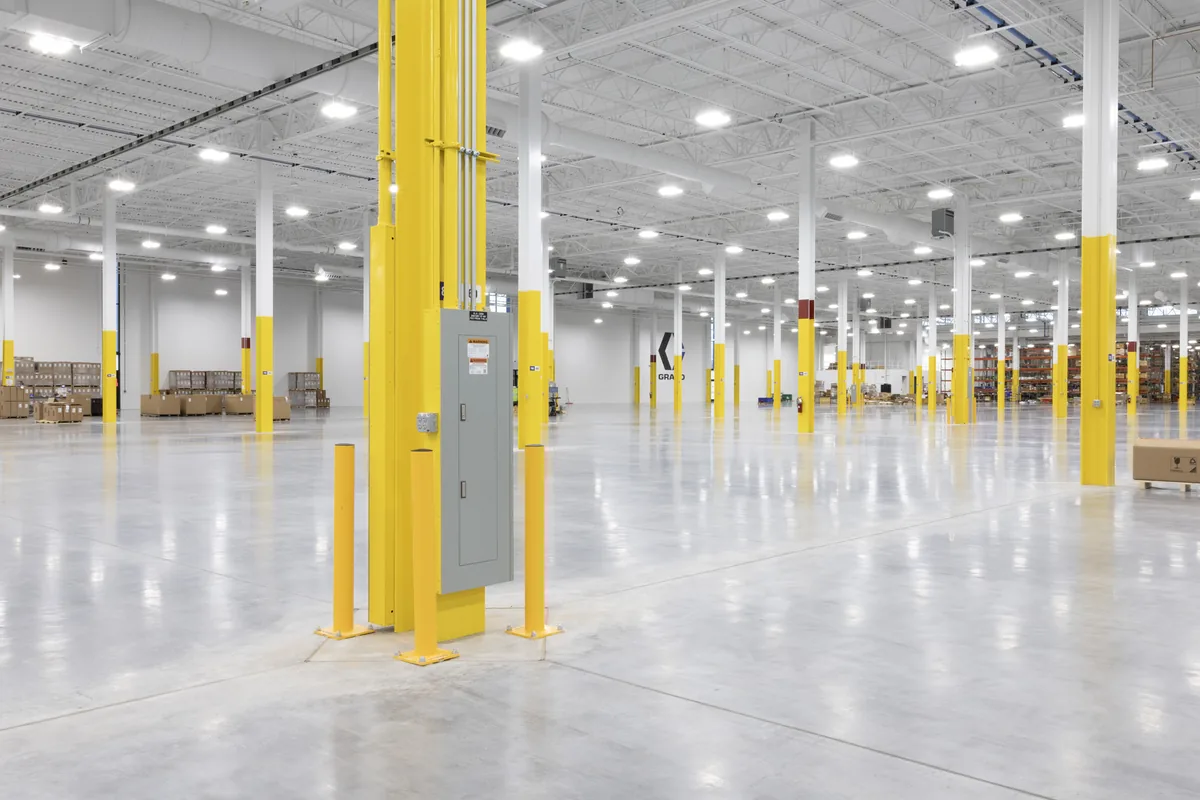 Ceiling lights and electrical distribution among yellow columns in a spacious warehouse.