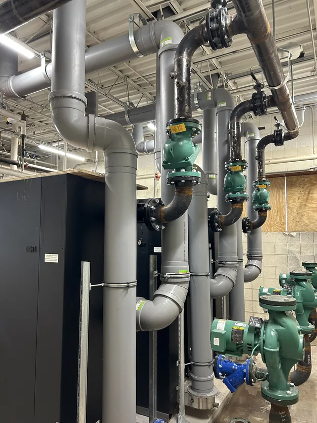 Installed piping, metal venting and green pumps in a mechanical room.