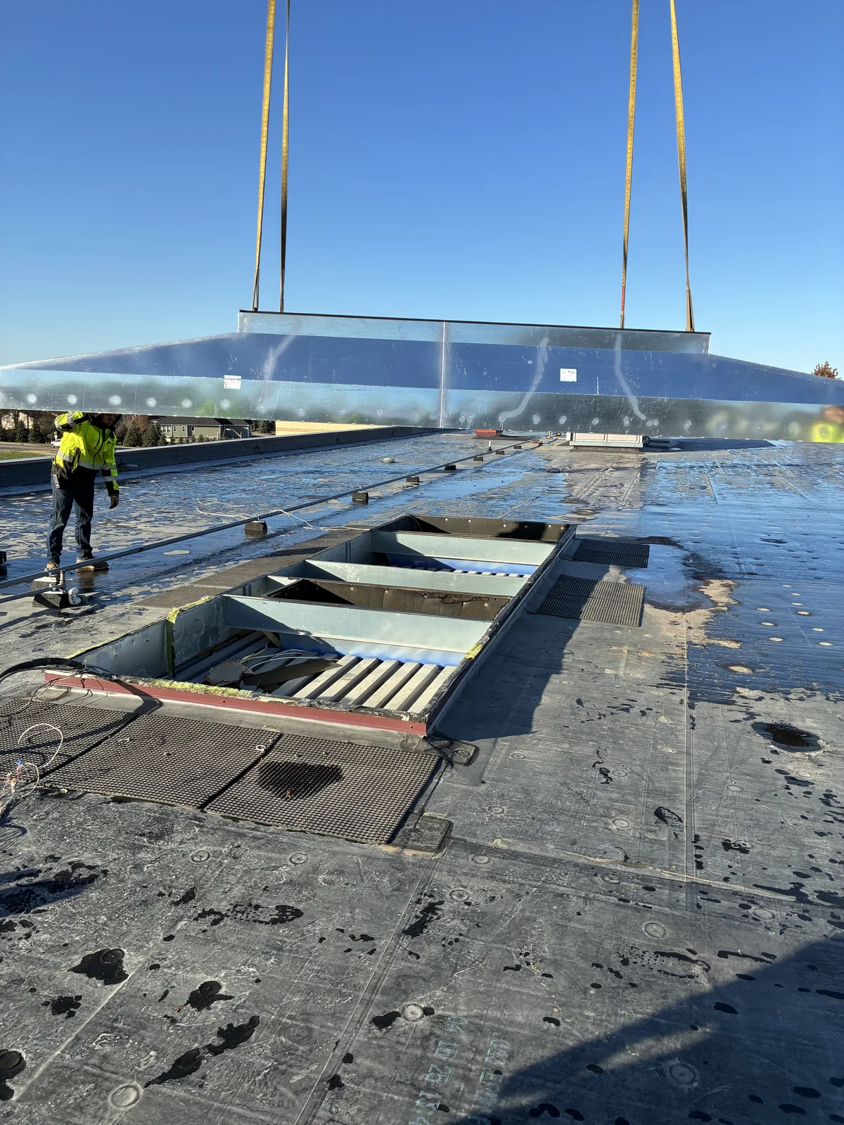 A custom fabricated metal curb being lifted into place over an opening in a commercial rooftop.