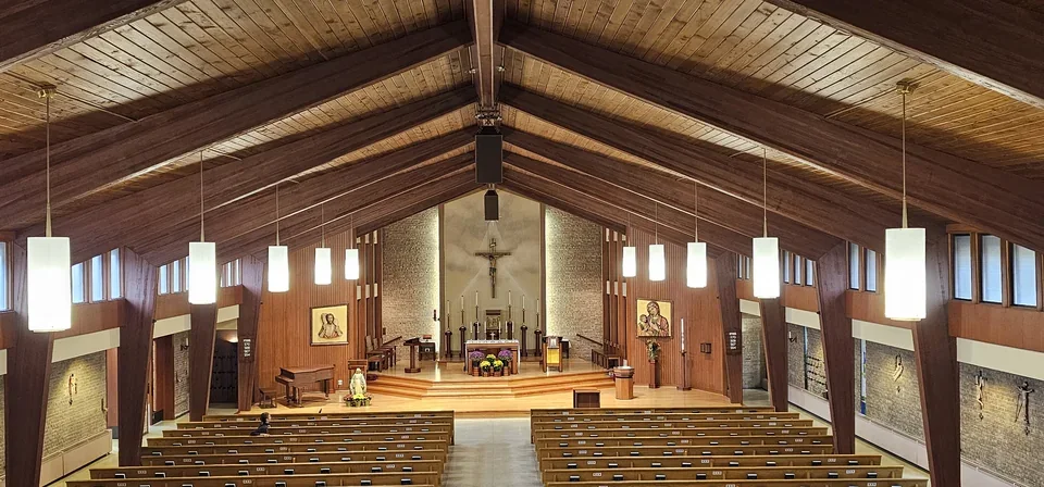 The interior of Good Shepherd Church, with wooden ceiling beams, suspended lighting and rows of seating.