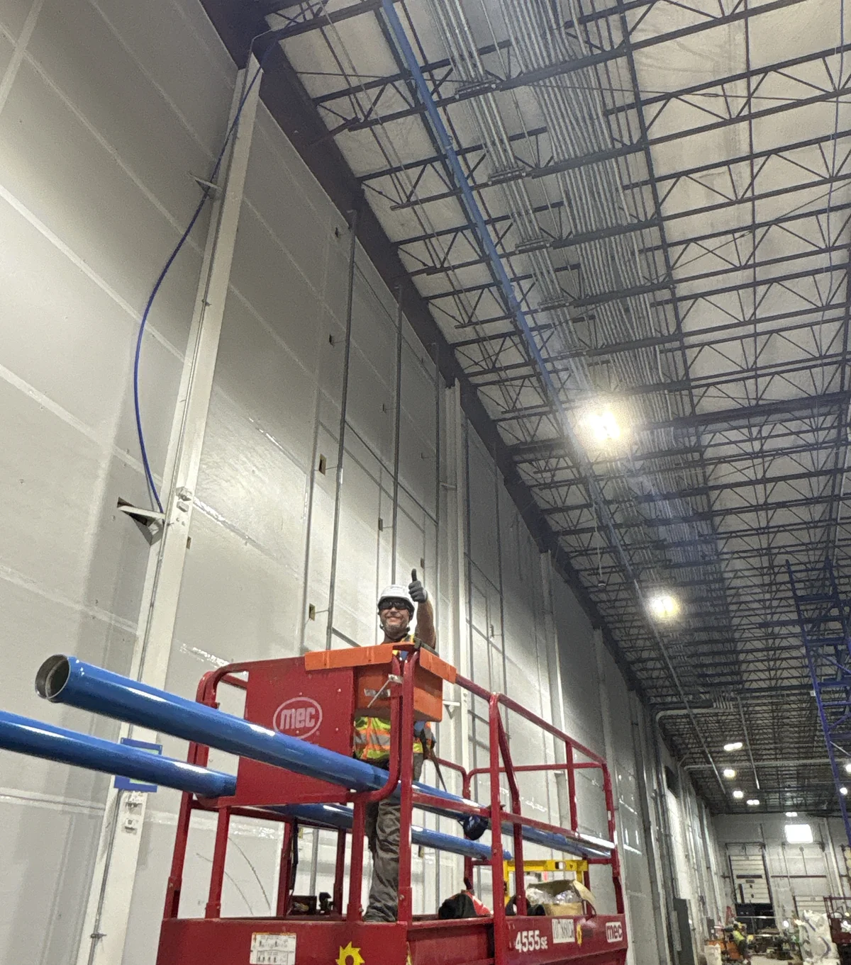 A plumbing installer working from an elevated platform beside blue piping at Walmart Distribution.