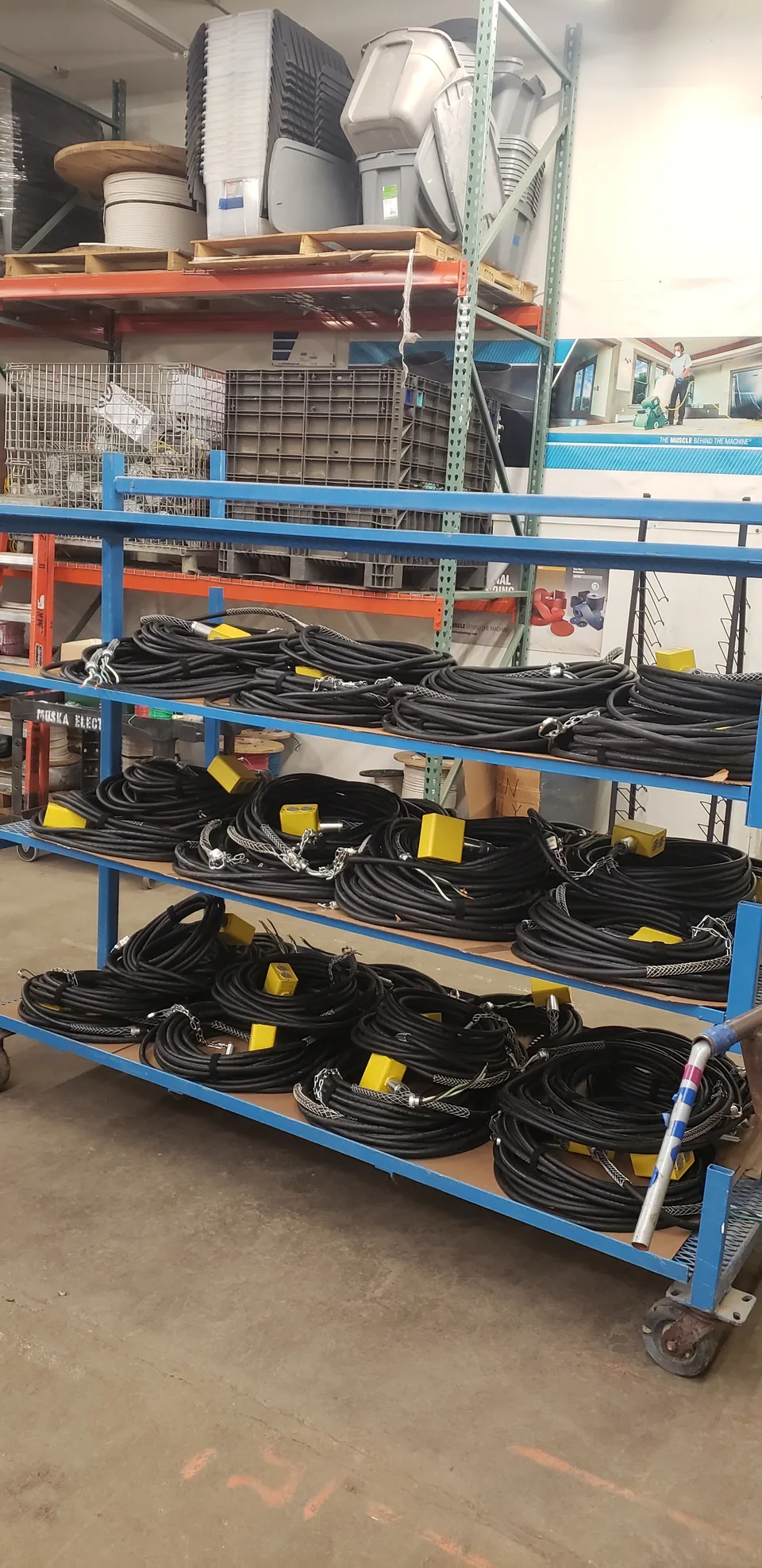 Coiled drop cord assemblies with yellow connectors organized on a blue rolling rack for Amazon in the pre-fabrication shop.