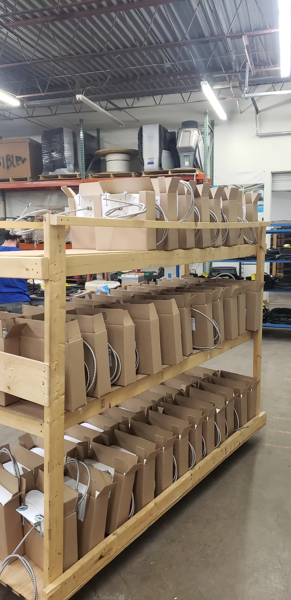 Emergency lighting assemblies with flexible conduit staged on a wooden rack for Costco in the pre-fabrication shop.