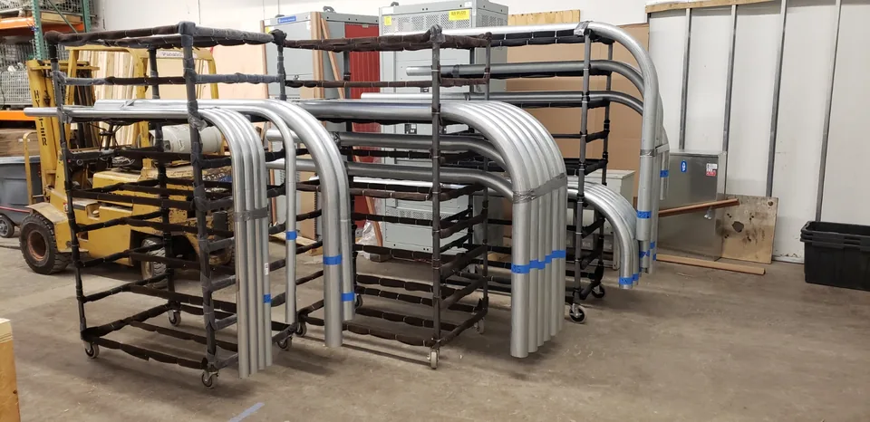 Rows of bent metal pipe organized on rolling racks in Muska's pre-fabrication shop.
